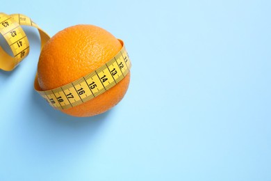 Photo of Cellulite problem. Orange with measuring tape on light blue background, top view. Space for text