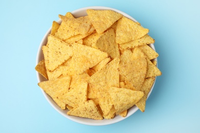 Photo of Bowl of tasty Mexican nachos chips on light blue background, top view