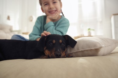 Photo of Little girl with cute puppy at home, focus on pet