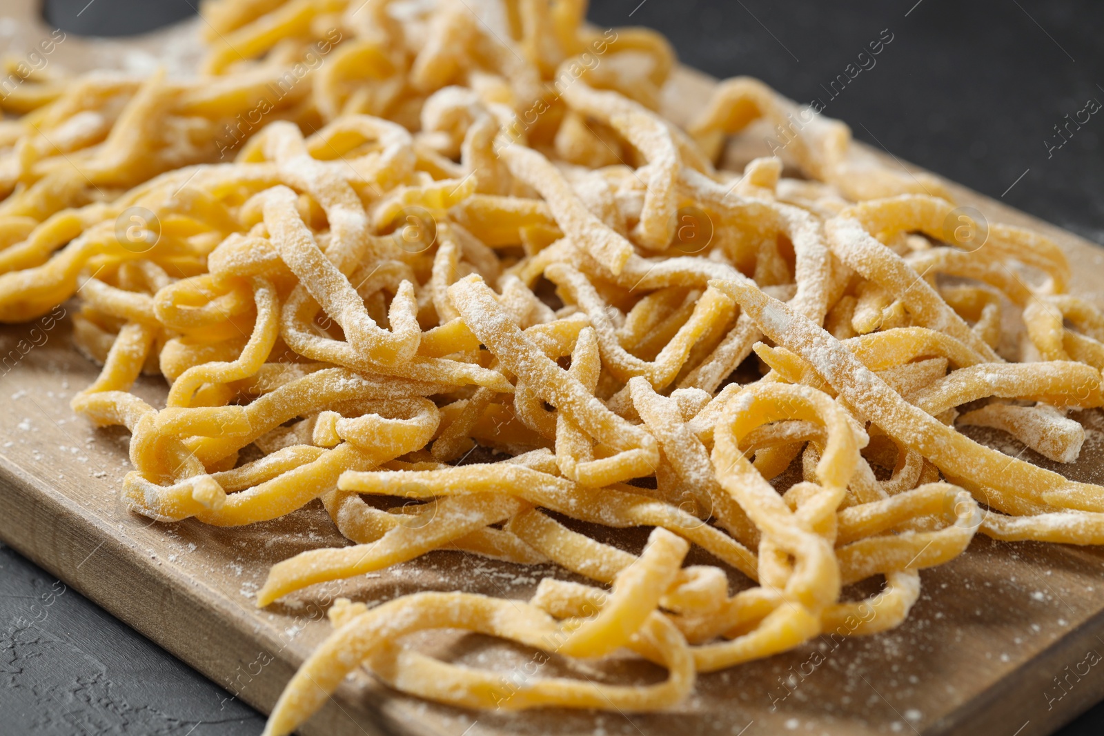 Photo of Board with homemade pasta and flour on dark table, closeup