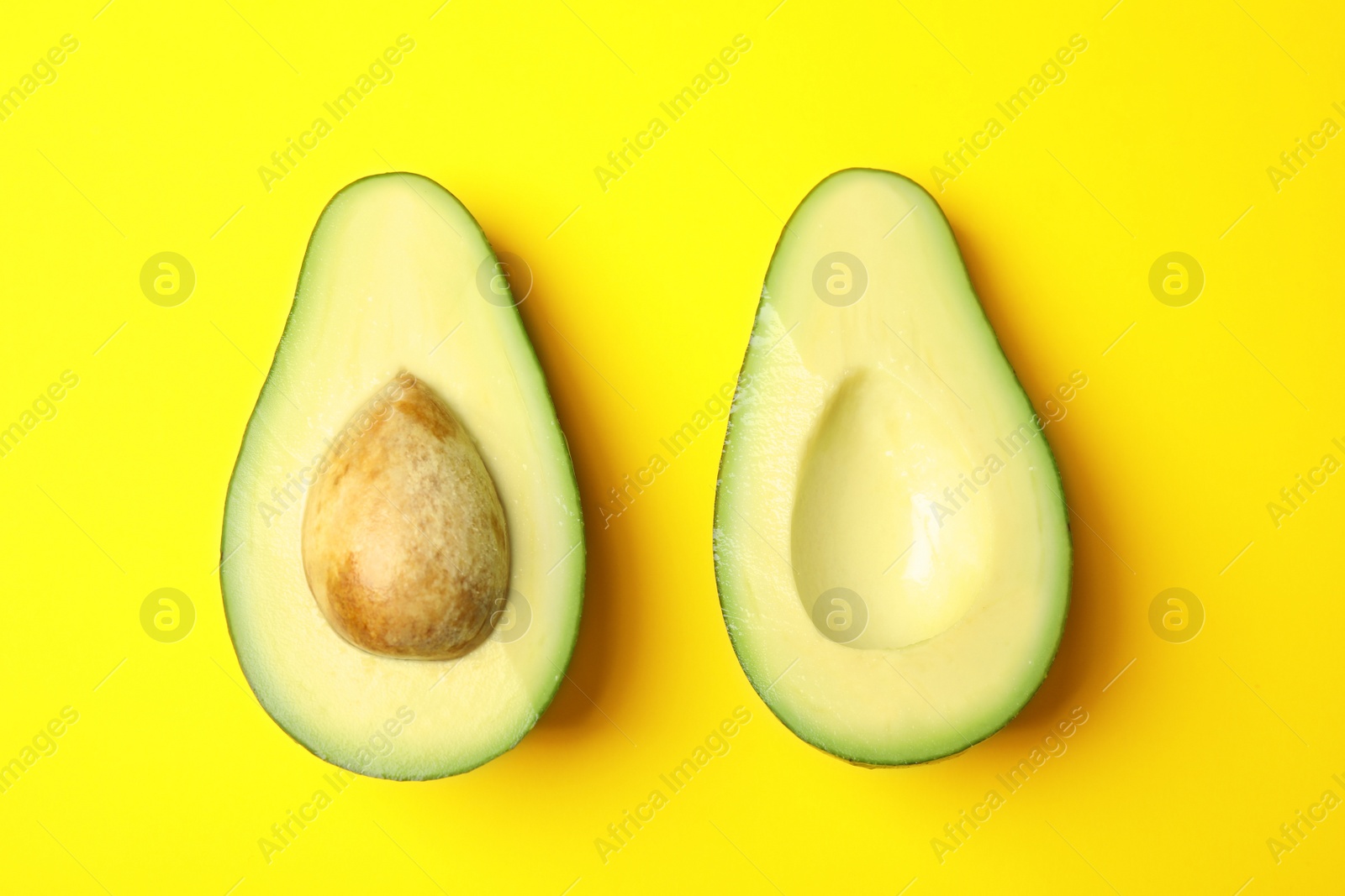 Photo of Cut fresh ripe avocado on yellow background, flat lay