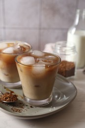 Photo of Refreshing iced coffee with milk in glasses, ingredients and spoon on light table, closeup