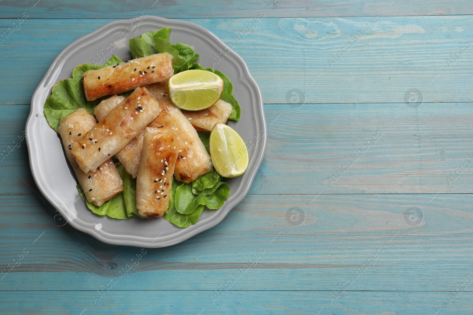 Photo of Tasty fried spring rolls on light blue wooden table, top view. Space for text