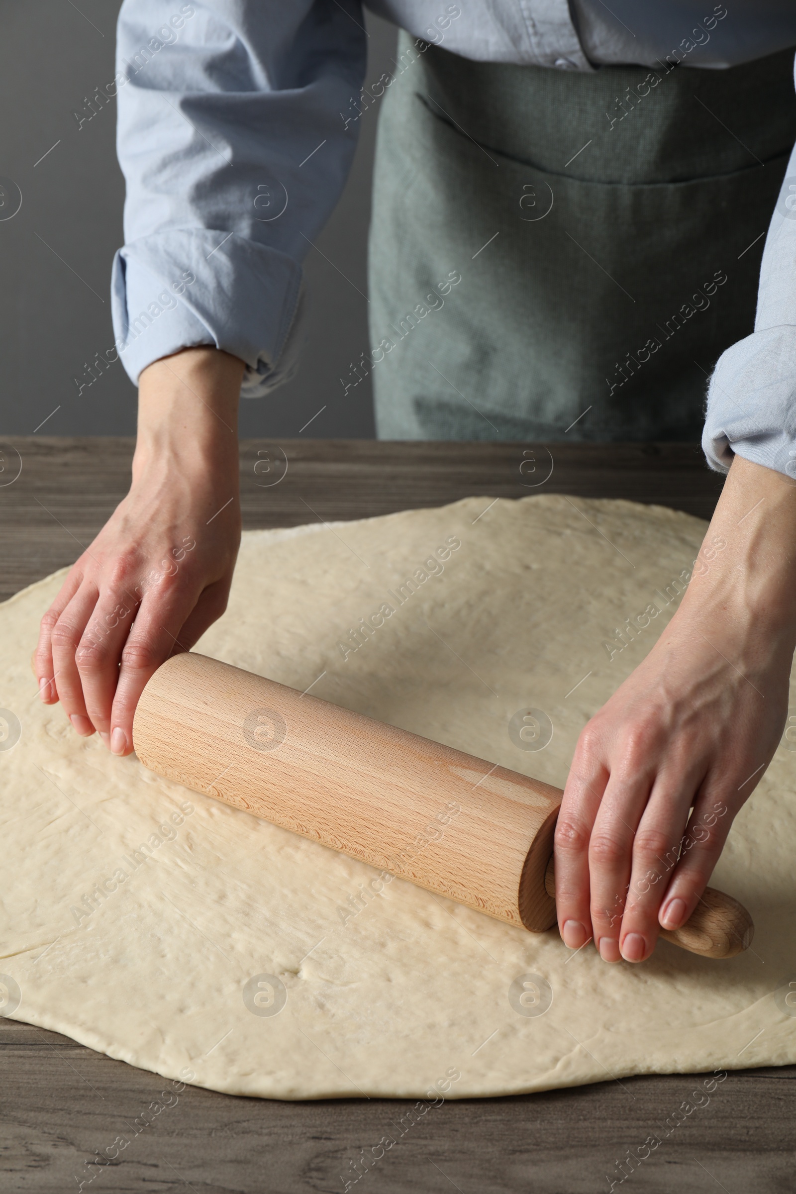 Photo of Woman rolling raw dough at wooden table, closeup