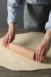 Woman rolling raw dough at wooden table, closeup