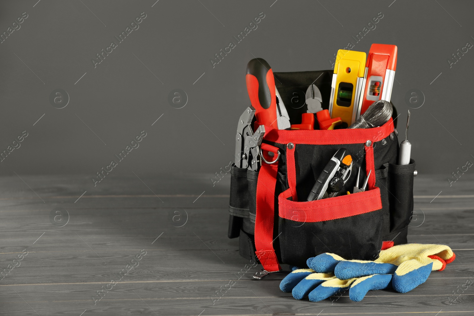 Photo of Bag with different tools for repair and protective gloves on wooden table, space for text