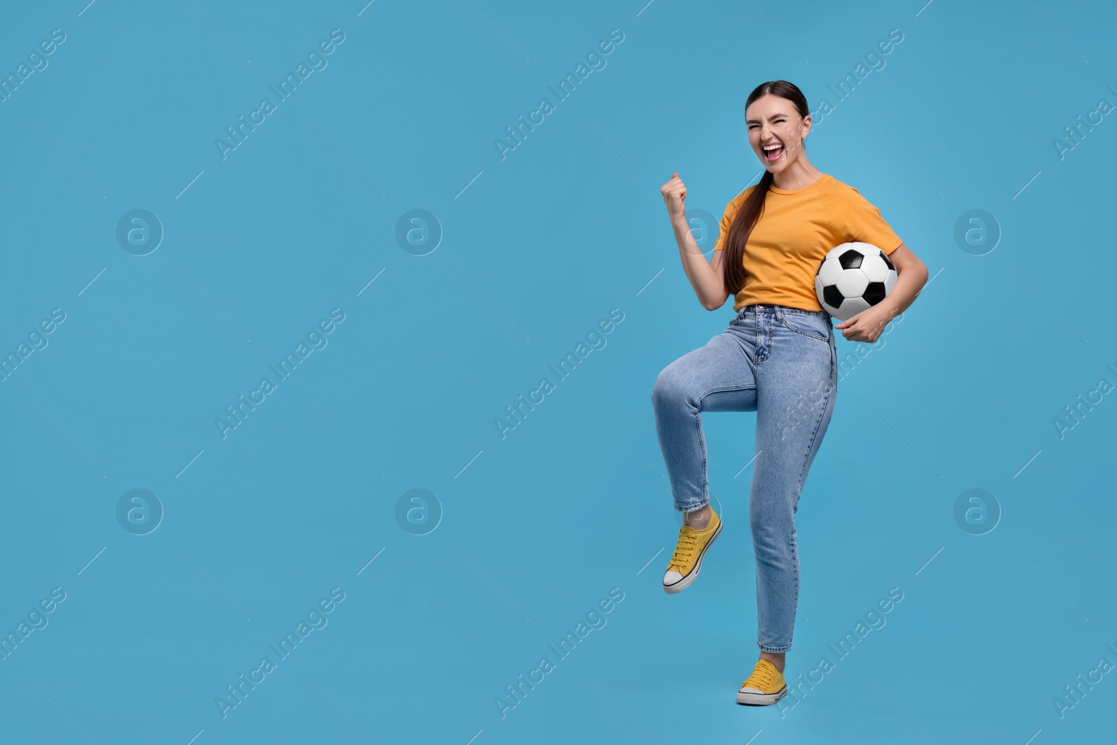 Photo of Happy soccer fan with ball celebrating on light blue background. Space for text