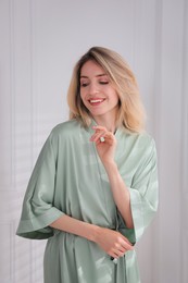 Photo of Pretty young woman in beautiful light green silk robe near white wall indoors