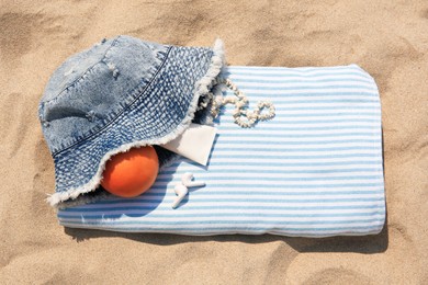 Photo of Denim hat, earphones, orange and beach accessories on sand, top view