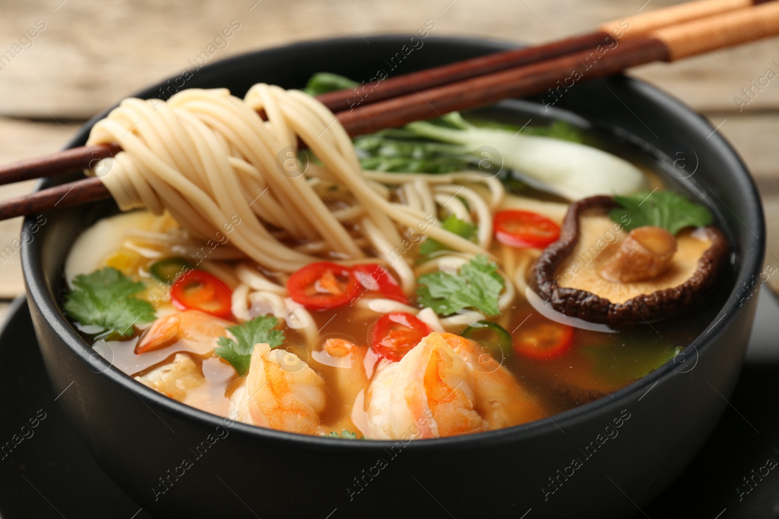 Photo of Bowl of delicious ramen with chopsticks on table, closeup. Noodle soup