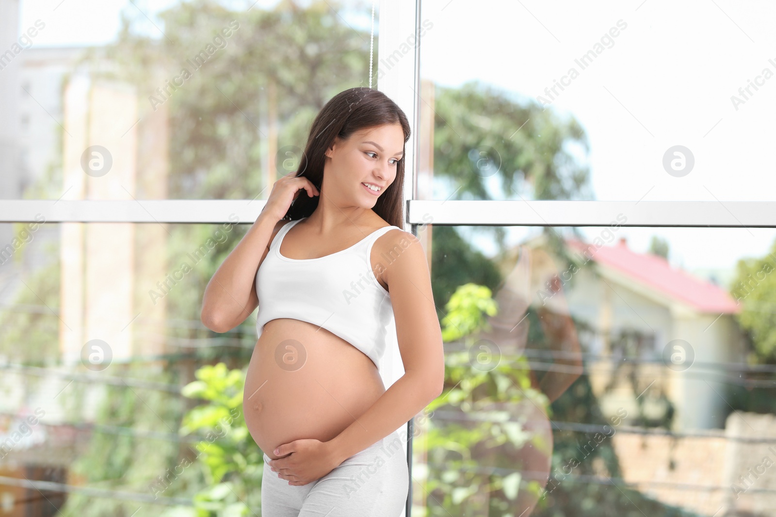 Photo of Happy pregnant woman standing near window at home