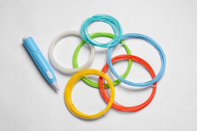 Photo of Stylish 3D pen and colorful plastic filaments on white background, flat lay