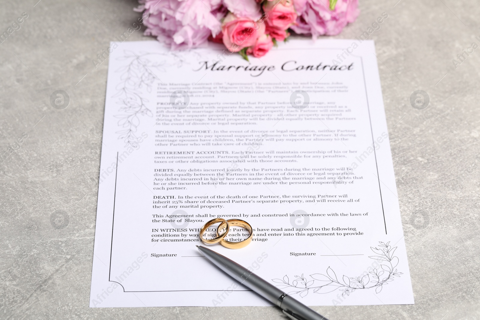 Photo of Marriage contract, golden wedding rings, pen and flowers on grey table