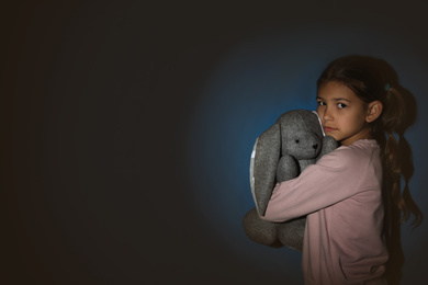 Sad little girl with toy near blue wall, space for text. Domestic violence concept