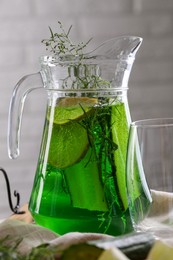 Photo of Jug of homemade refreshing tarragon drink with lemon slices and cucumber on table, closeup