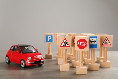 Photo of Many different miniature road signs and car on grey table, space for text. Driving school