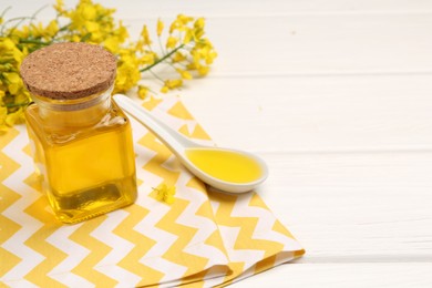 Rapeseed oil in glass bottle, gravy boat and beautiful yellow flowers on white wooden table, space for text
