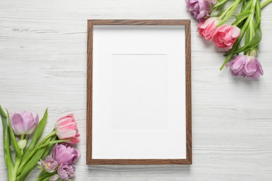 Photo of Empty photo frame and beautiful flowers on white wooden table, flat lay. Space for design