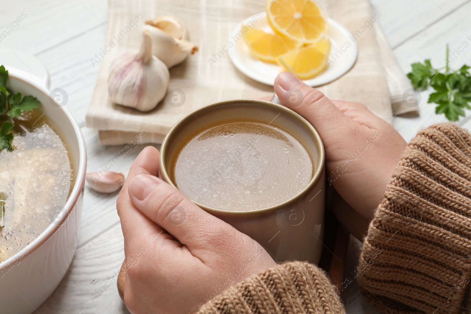 Photo of Woman with cup of hot delicious bouillon at white wooden table, closeup