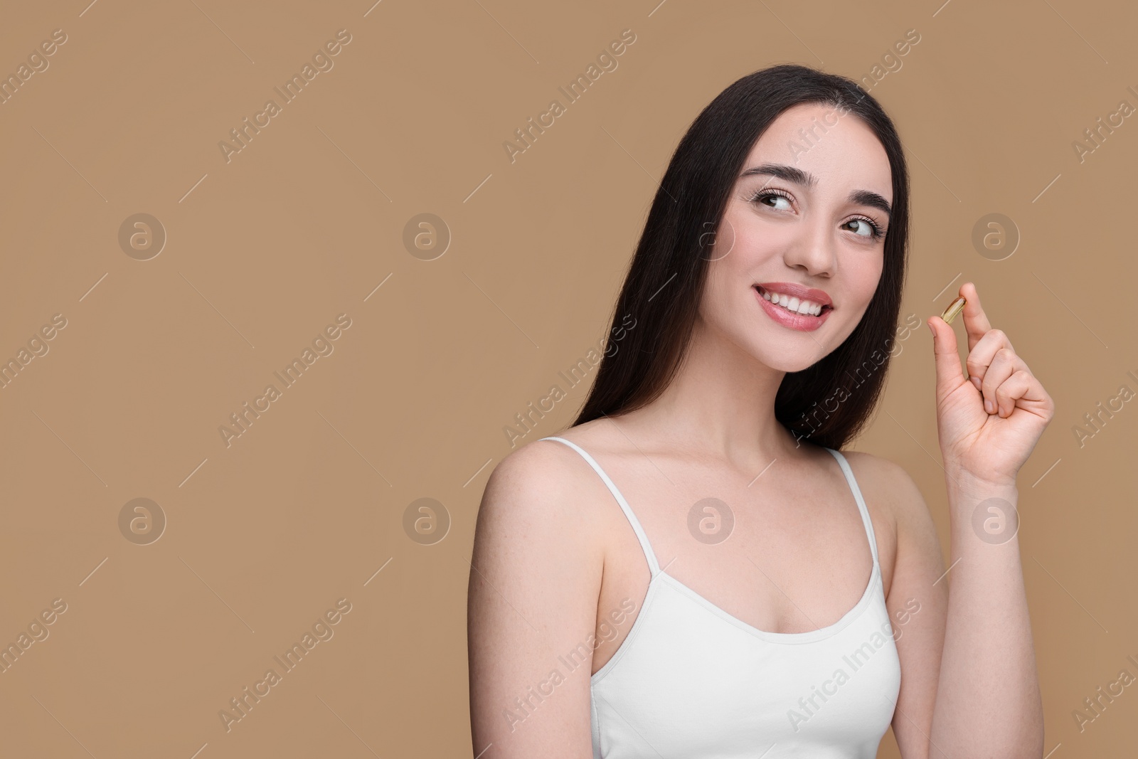 Photo of Beautiful young woman with vitamin pill on beige background. Space for text