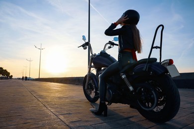 Photo of Woman in helmet sitting on motorcycle at sunset. Space for text