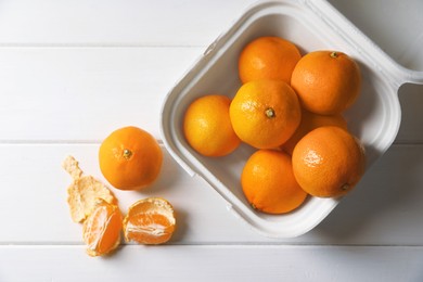 Photo of Paper box with fresh ripe tangerines on white wooden table, flat lay