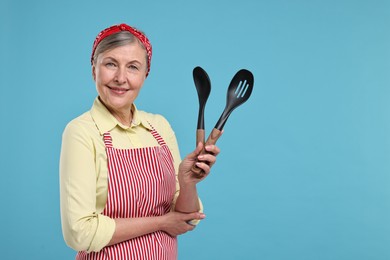 Happy housewife with spoons on light blue background, space for text