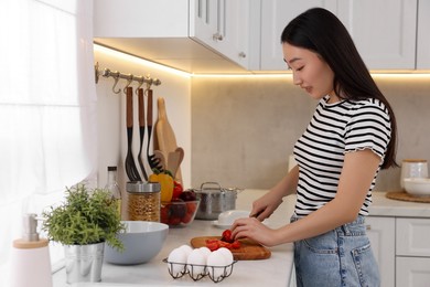 Photo of Cooking process. Beautiful woman cutting tomato in kitchen