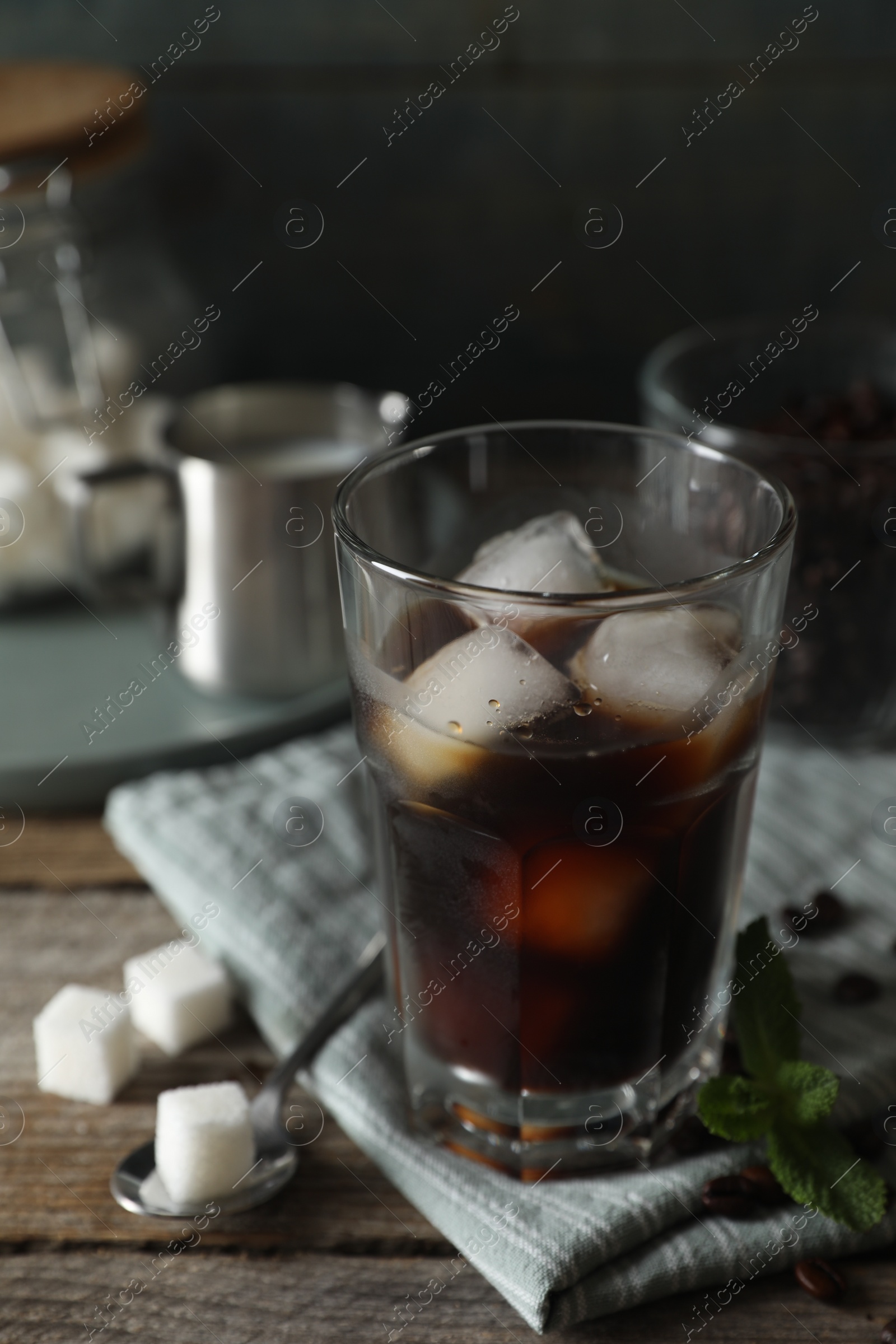 Photo of Glass of delicious iced coffee, mint and sugar cubes on wooden table