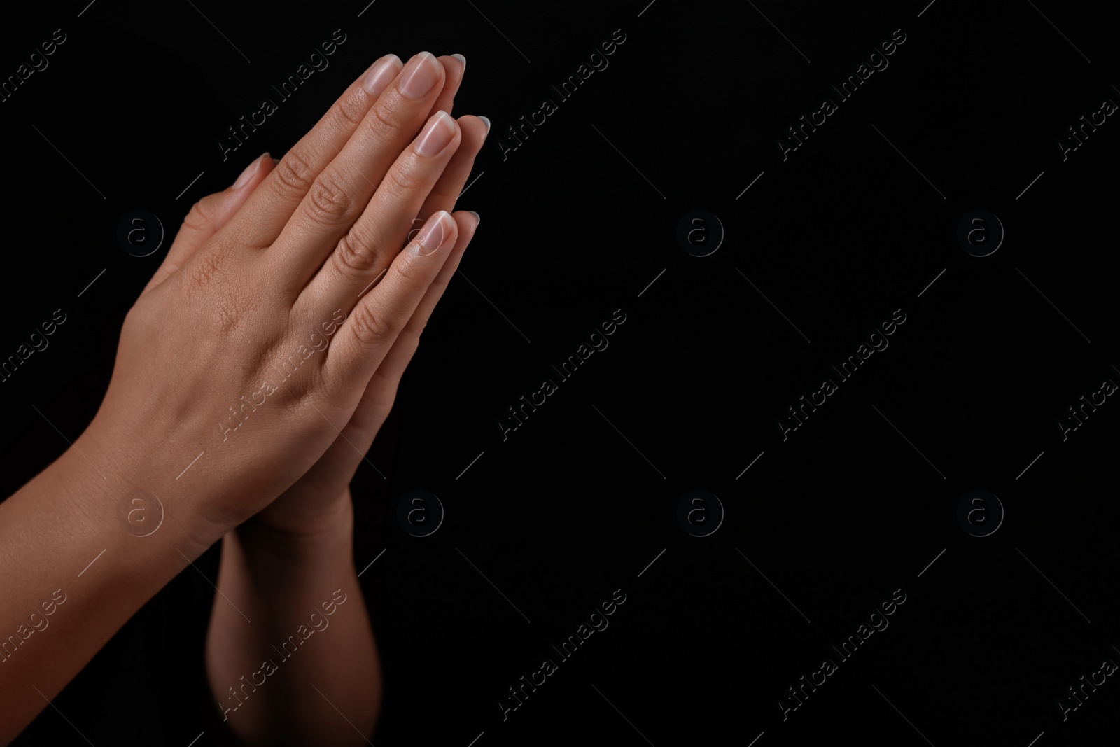 Photo of Woman holding hands clasped while praying against black background, closeup. Space for text