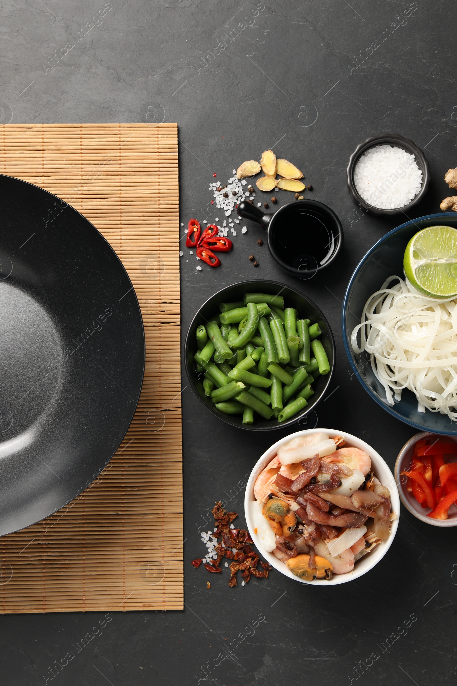 Photo of Flat lay composition with black wok, spices and products on dark textured table