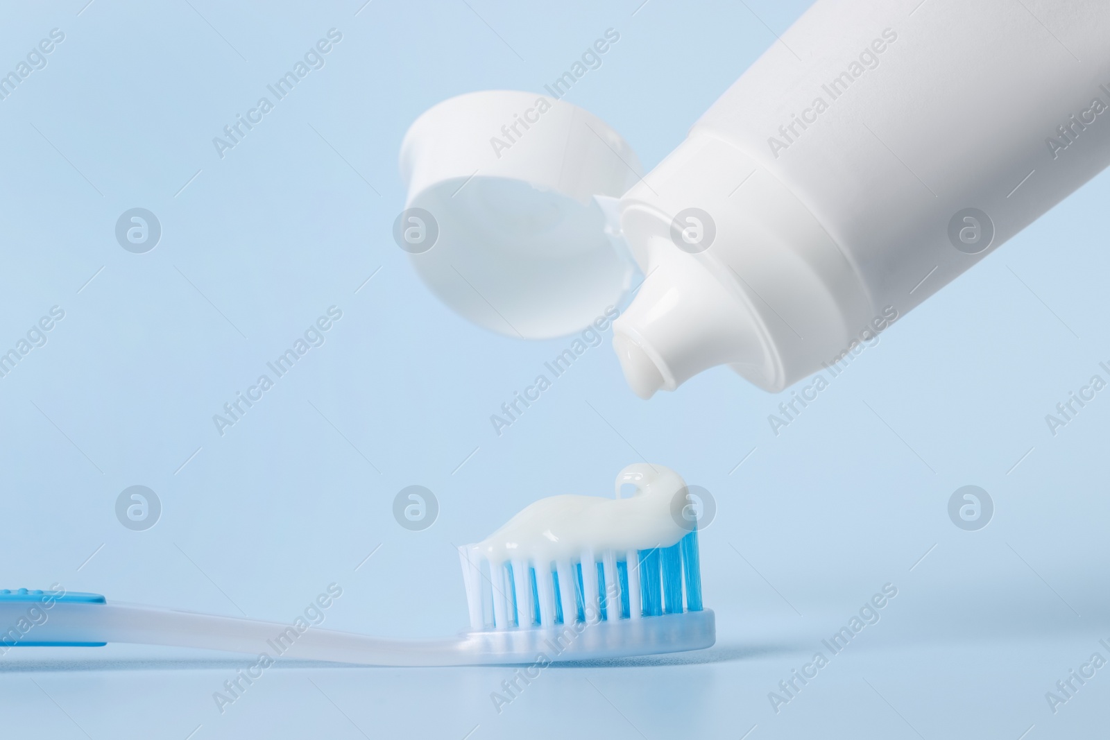 Photo of Applying paste on toothbrush against light blue background, closeup