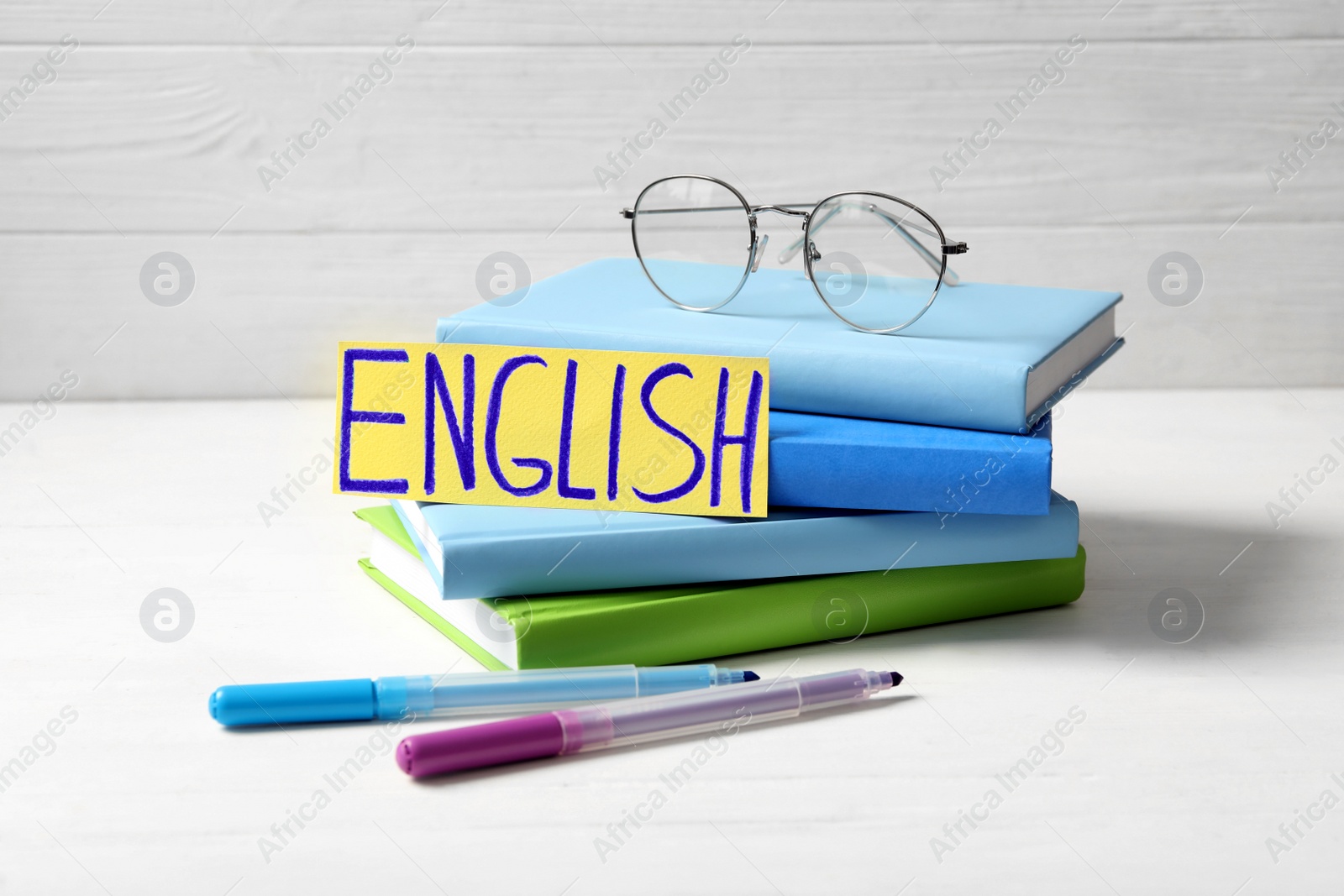 Photo of Word ENGLISH, books, glasses and felt tip pens on white wooden table