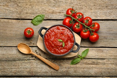 Photo of Homemade tomato sauce in bowl, spoon and fresh ingredients on wooden table, flat lay