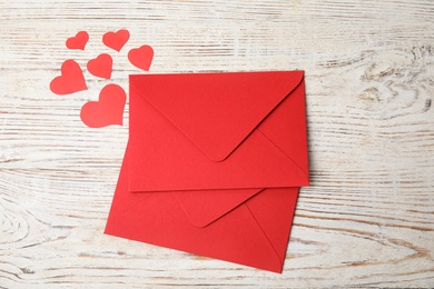Red envelopes and paper hearts on white wooden table, flat lay. Love letters