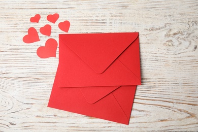 Photo of Red envelopes and paper hearts on white wooden table, flat lay. Love letters