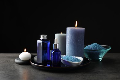 Photo of Spa composition. Cosmetic products, burning candles and sea salt on gray table against black background