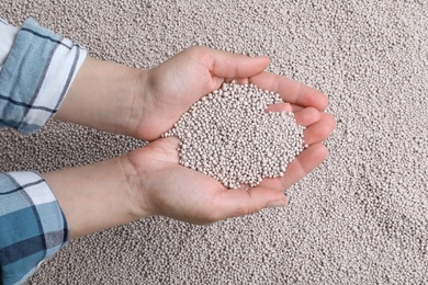 Woman holding chemical fertilizer over pellets, closeup. Gardening season