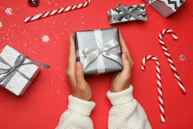 Photo of Young woman holding Christmas gift on red background, flat lay