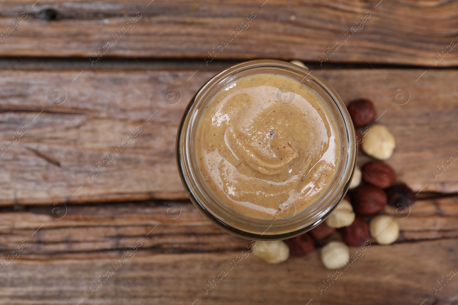 Photo of Tasty hazelnut nut paste in jar on wooden table, top view. Space for text