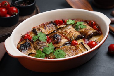 Tasty eggplant rolls with tomatoes, cheese and parsley in baking dish on black table, closeup
