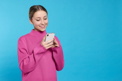 Photo of Teenage girl using smartphone on light blue background. Space for text