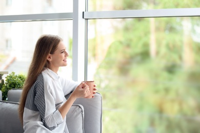 Photo of Young beautiful woman drinking morning coffee near window at home