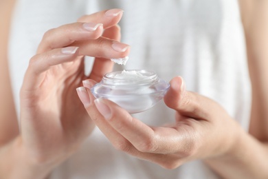 Young woman holding glass jar of cream, closeup