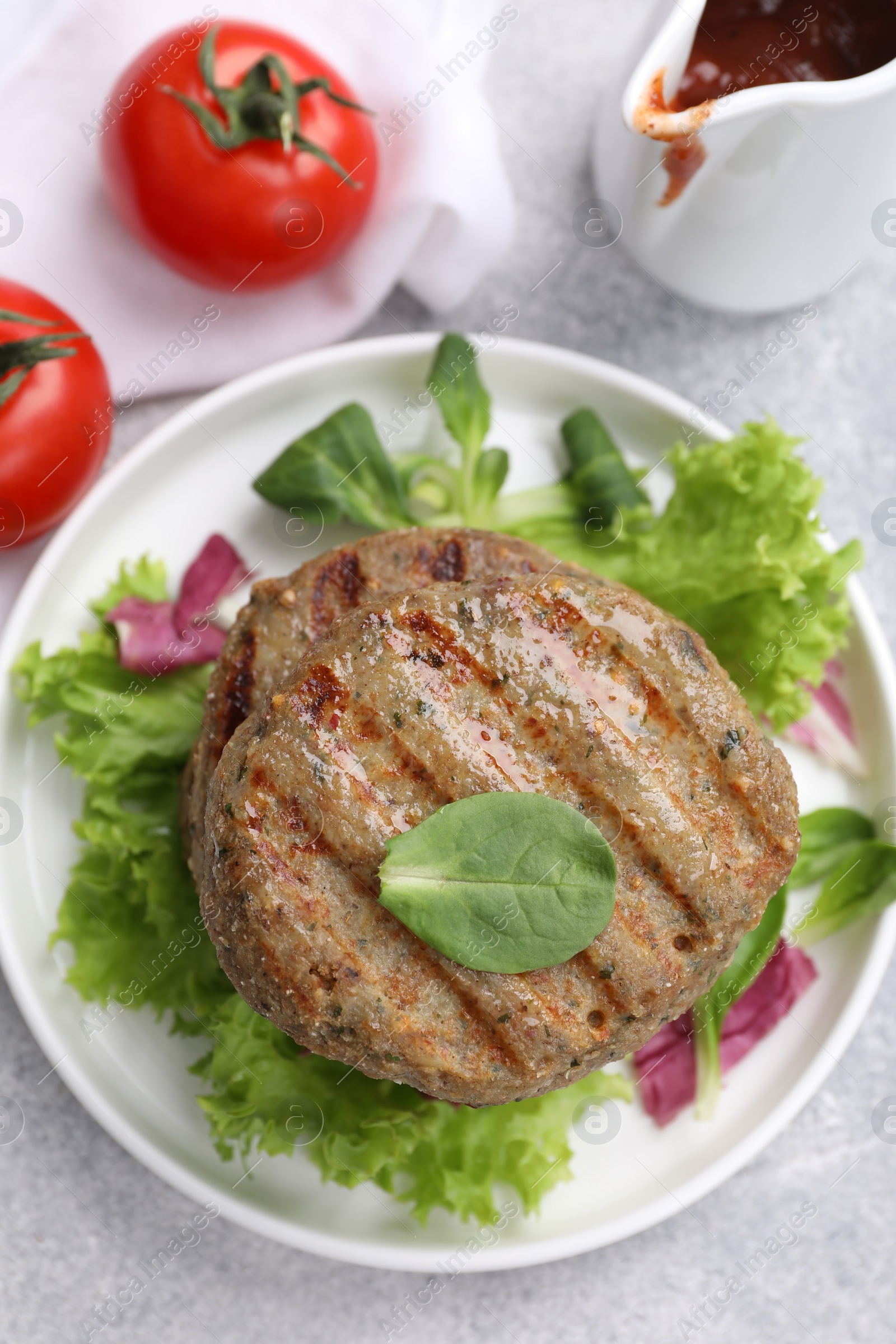 Photo of Delicious vegan cutlets, lettuce, spinach and tomatoes on light grey table, closeup