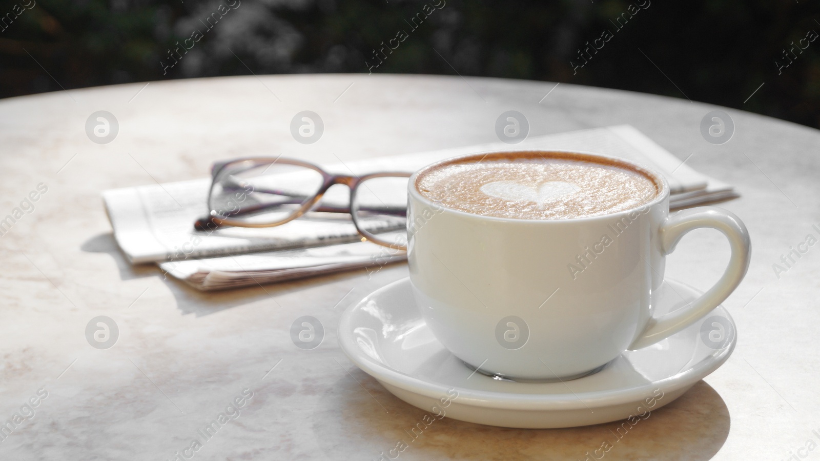 Photo of Cup of delicious coffee, glasses and newspaper on beige marble table outdoors, space for text