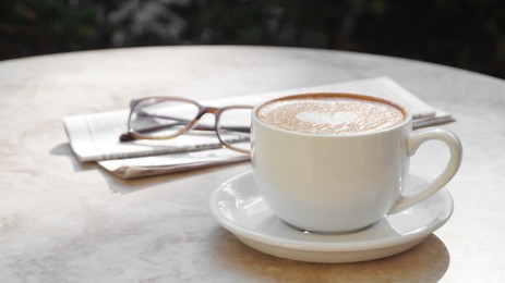 Cup of delicious coffee, glasses and newspaper on beige marble table outdoors, space for text