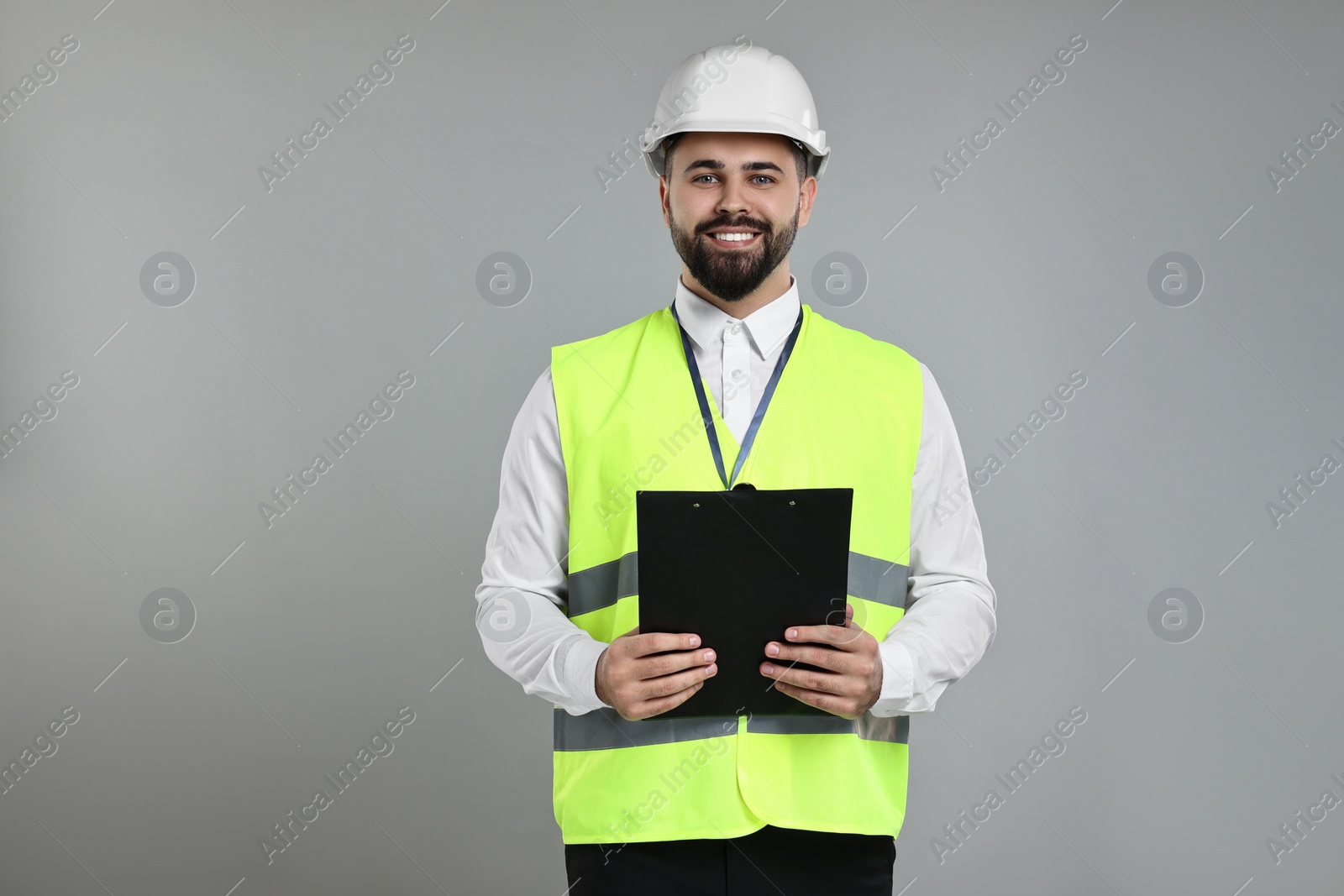 Photo of Engineer in hard hat holding clipboard on grey background