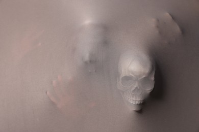 Silhouette of creepy ghost with skulls behind grey cloth