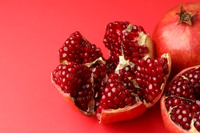 Photo of Whole and cut fresh pomegranates on red background, closeup